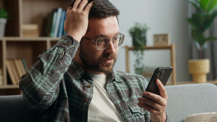 Caucasian man male guy user at home browsing mobile phone app social media smartphone shock bad...