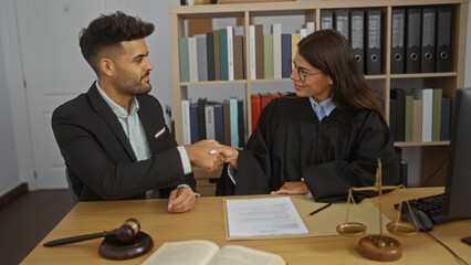 Man and woman in professional attire shaking hands in an office setting with legal documents and a gavel on the desk.