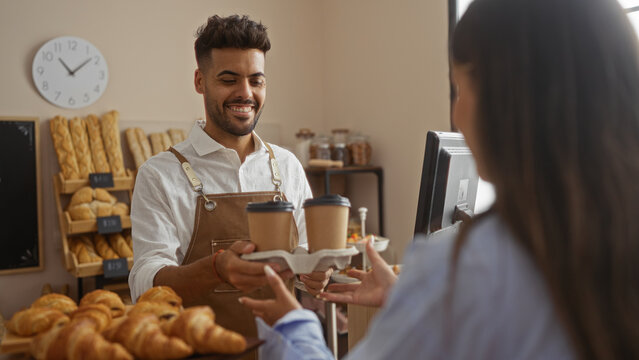 Man serving coffee to woman in bakery with shelves of bread in the background and a clock on the wall