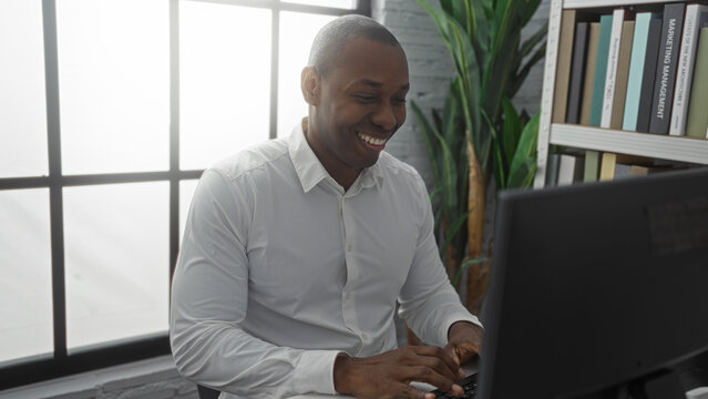 Young man working indoors in office setting with smile and focus, displaying professional atmosphere enhanced by bookshelves and plants.