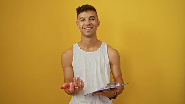 Smiling young hispanic man holding clipboard and pen in front of vibrant yellow wall, showcasing an approachable and professional demeanor.