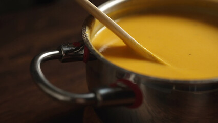 Pumpkin soup in a saucepan. Stirring with a wooden spoon.