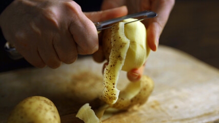 A woman peels potato using a vegetable peeler.