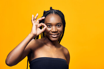 Fototapeta premium Young Black woman with braided hair giving an OK sign against a bright yellow background, exuding positivity, confidence, and joy in a vibrant setting