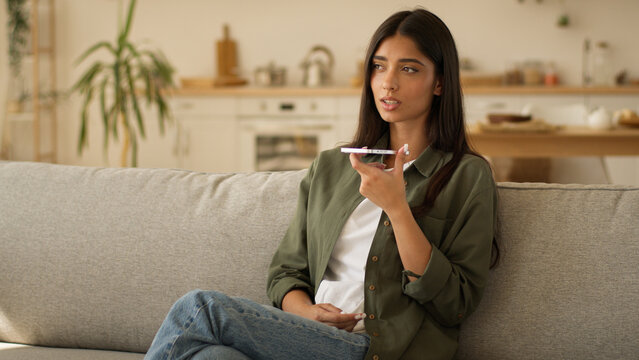 Muslim woman Arabian girl Islamic lady female talking mobile phone loudspeaker dictate talk speech speak to smartphone microphone call record audio message recording voice mail at home couch kitchen