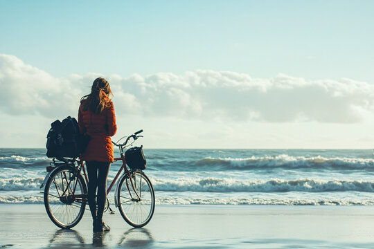a woman standing on the beach with a bike
