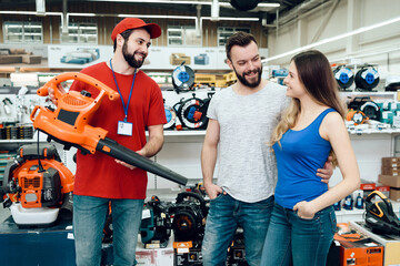 Salesman is showing couple of clients new leaf blower in power tools store.