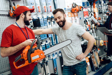 Two salesmen in red shirt and baseball cap are showing female client new rake in power tools store.
