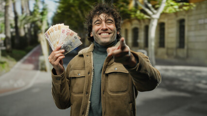 Hispanic man enthusiastically holding turkish lira outdoors on a lively city street, showcasing...