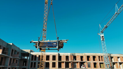 Tower crane lifting construction materials at a building site with workers and scaffolding.