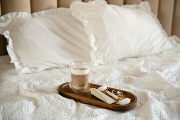 A serene bedroom scene with soft pillows, a glass of coffee, and spa essentials elegantly arranged on a wooden tray on white bed.