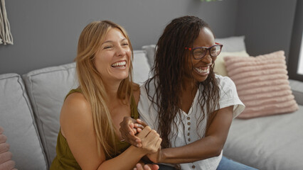 Women laughing together on a sofa in a cozy living room, showcasing friendship and happiness in a comfortable home environment