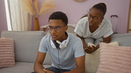 Fototapeta premium Woman talking to her son indoors at home, they are sitting on a couch in the living room which is decorated with pink pillows and dried plants, family bonding moment.