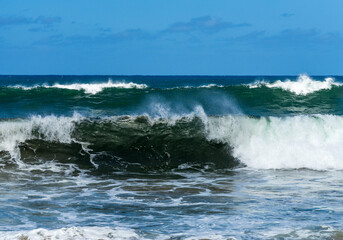 Ocean waves crashing on the shore under a blue sky, with the turquoise water rippling and splashing at Lumahai Beach.