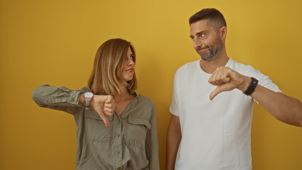 Man and woman giving thumbs down in front of yellow background showing disapproval or disagreement together