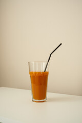 A refreshing glass of vibrant pumpkin juice with straw on white table.