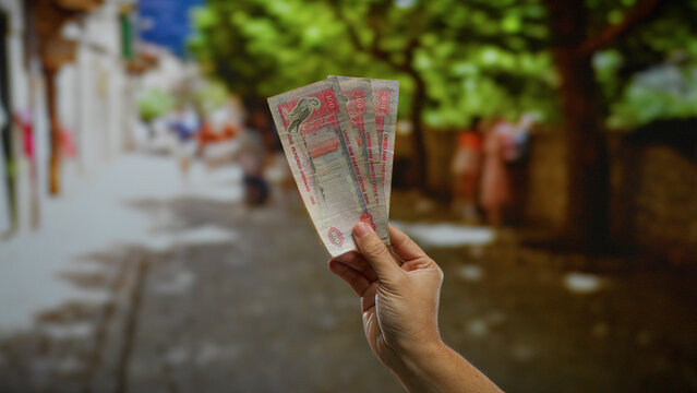 Man holding uae dirham banknotes on urban street with blurred background, showcasing currency, finance, and travel in a vibrant city setting in the united arab emirates.