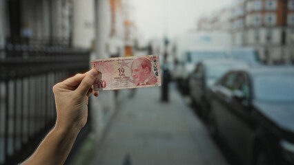 Man holding a turkish lira banknote outdoors on a city street, capturing urban life and financial...