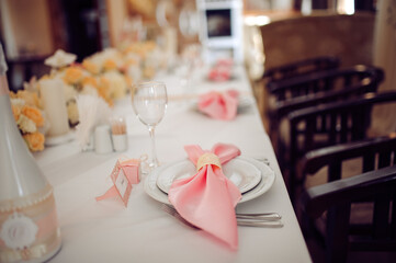 Wedding table with pink napkins, white plates, floral centerpiece, and place cards.