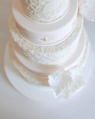 Detailed view of a white tiered wedding cake with lace patterns and floral decorations.