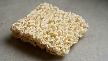 Stock image showcasing a block of uncooked instant noodles on a gray surface, highlighting texture and simplicity.