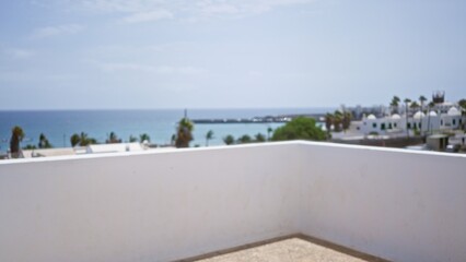 Blurred view of the lanzarote coastline with white buildings, palm trees, and the ocean under a clear sky.