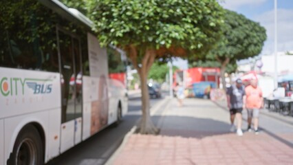 Blurred image of two men walking near a city bus in lanzarote, spain, showcasing a defocused outdoor sidewalk scene with trees and background bokeh.