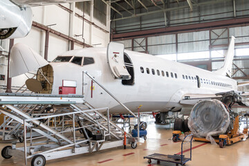 White passenger aircraft under maintenance has opened weather radar and engine removed located nearby in the airplane hangar