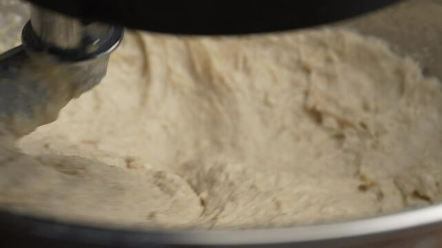 Kneading elastic dough for bread in a kneading machine in a bakery, close up. Mixer for kneading dough. Kneading yeast-free dough from whole grain and rye flour