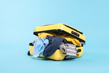 Packed suitcase full of clothes on light blue background
