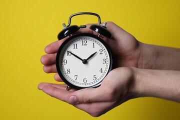 Man with alarm clock on yellow background, closeup
