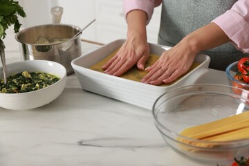 Woman making spinach lasagna at marble table indoors, closeup