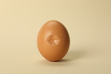One egg with cracked shell on beige background, closeup