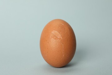 One egg with cracked shell on light grey background, closeup