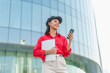 Young Asian Woman Holding Laptop and Phone Outside Office Building
