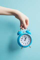A blue alarm clock holds a hand in the background of a blue background. Vertical photography. A...