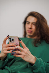Non-binary person using their cell phone at home with blurred background. Long nails.