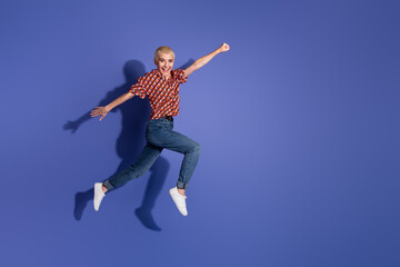 Obraz premium Cheerful young woman jumping mid-air over a vibrant purple backdrop emphasizing energy and positivity