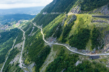 Winding mountain road cutting through steep green slopes. Aerial view highlights the remote and...