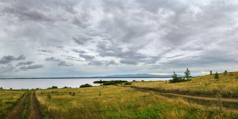 Summer cloudy landscape, mountains at the horizon and a field path leading to the lake, summer...