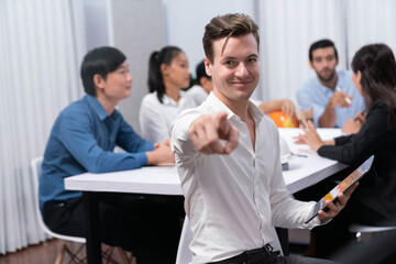 Confidence and happy smiling businessman portrait with background of his colleague and business team working in office. Office worker teamwork and positive workplace concept. Prudent