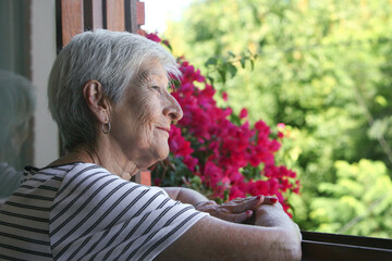 portrait of senior latino woman looking through the window at her garden 