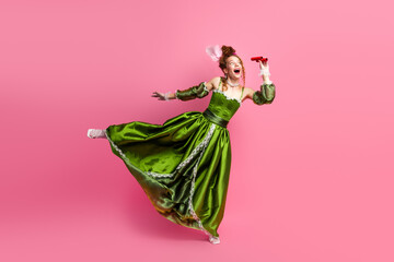 Elegant woman in green baroque-style dress contrasting modern era life on pink background