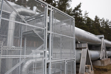 Naklejka premium pipeline and pipeline elements behind a metal fence and mesh against the background of a forest and gray sky