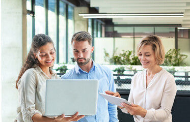 Three business people discussing work together using laptop and tablet in a modern office