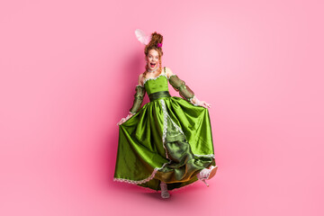 Elegant young woman in a green baroque gown posing against a pink backdrop, embodying classic...