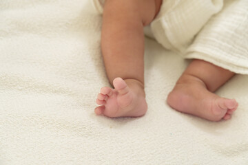 Asian newborn baby is lying on a bed. Baby gazing at mother, sucking on tiny hand. Deep eye contact...