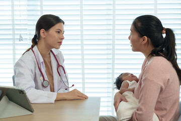Asian mother brings newborn son to see pediatrician. Female doctor and young mother discuss baby's...