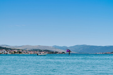 A talented windsurfer maneuvers effortlessly across sparkling blue waters, backed by gentle hills...