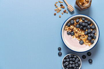Bowl with blueberry greek yogurt and oat granola on light blue background with copy space. Food...